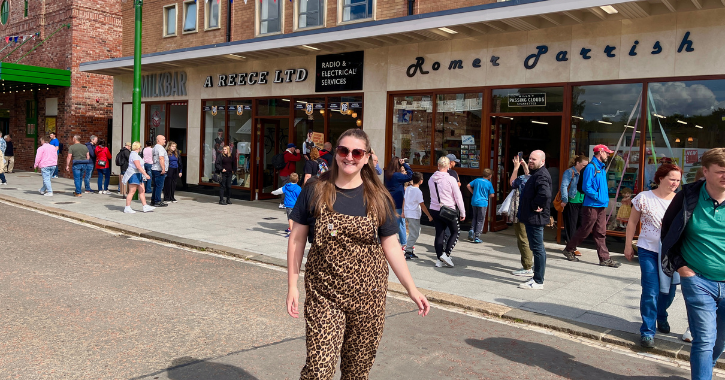 woman standing smiling at camera in the middle of the 1950s town street at Beamish Museum